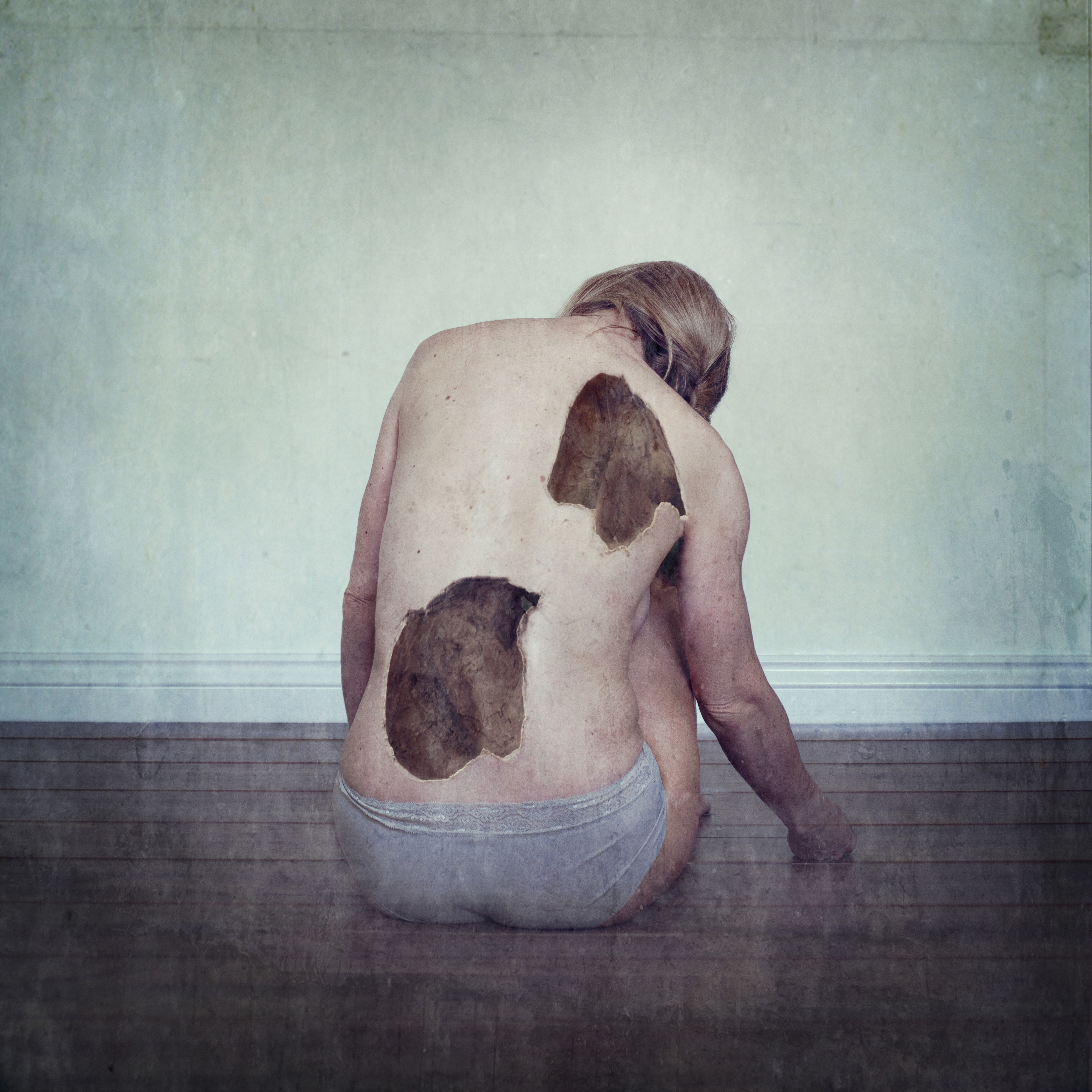Woman sits on floor with her back facing. there are two larges holes in her back.
